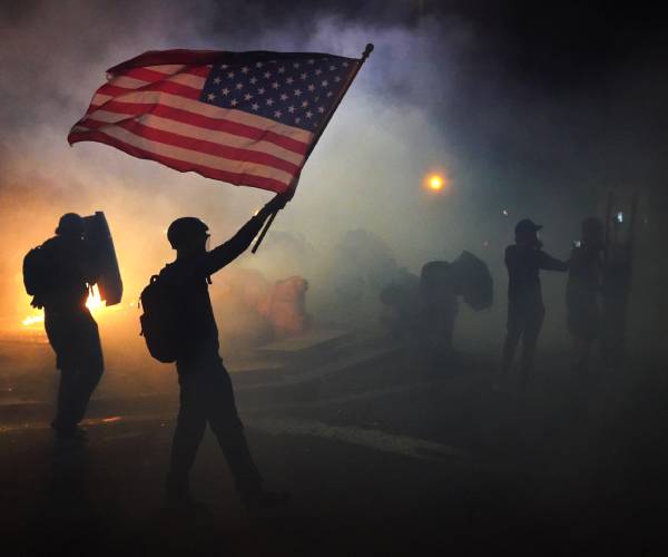 a protester walks through tear gas holding an american flag