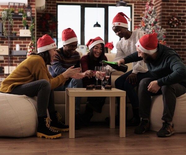 men and women in an office with santa hats on drinking champagne