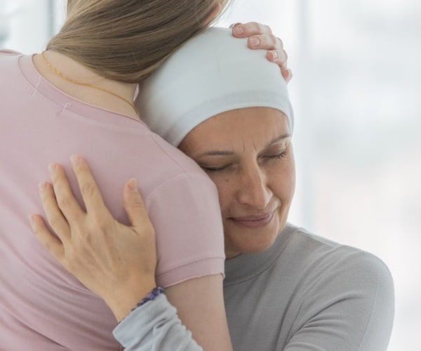 young woman with scarf on head due to chemo hair loss hugging a friend