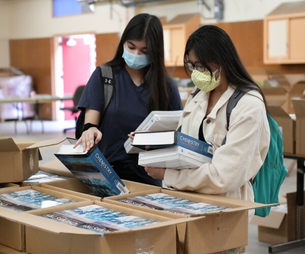 two girls pick up chemistry textbooks wearing masks