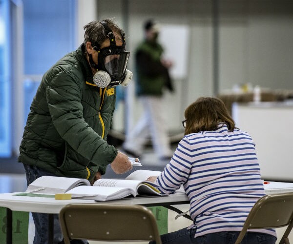 a man is shown wearing a full face chemical mask as he prepares to vote