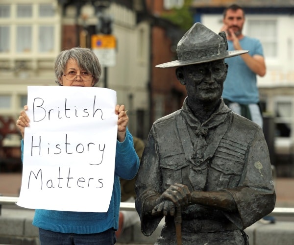 woman with british history matters poster stands next to the statue of baden-powell