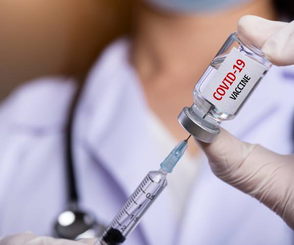 a medical professional drawing a covid vaccine from a vial into a syringe