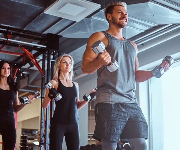 A man and two women in an exercise class lifting weights