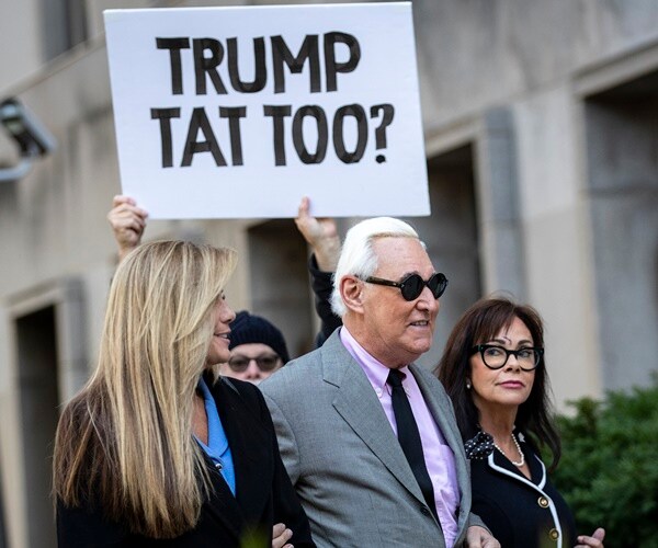 roger stone walks into court with a protester behind him, referencing a pardon