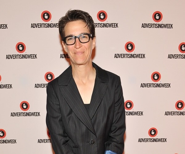 rachel maddow stands against a wall