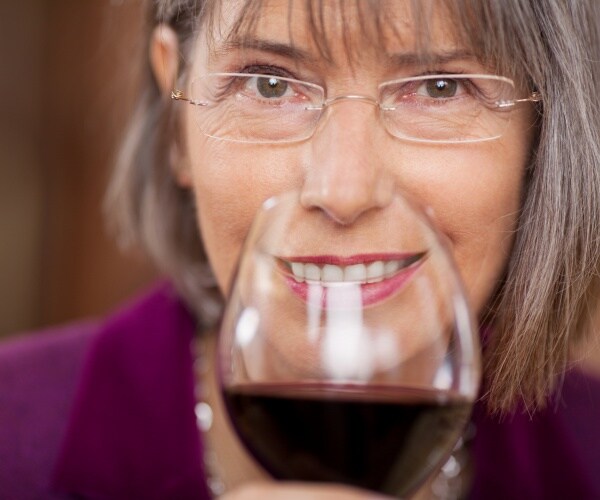 woman smiling at camera drinking red wine out of large wine glass