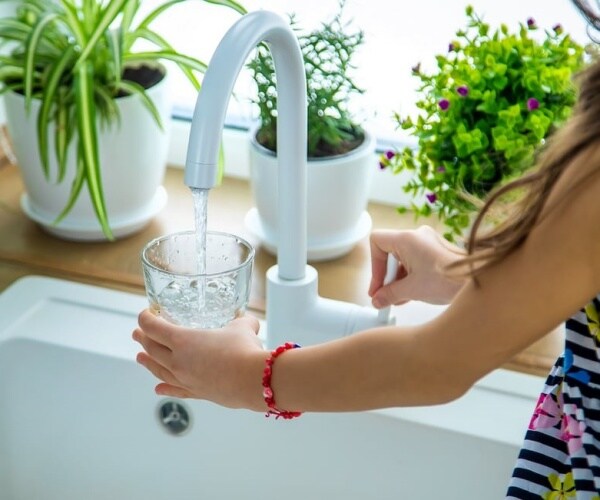 woman filling water in glass from faucet in sink