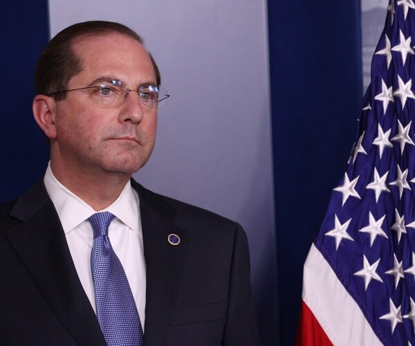 Alex Azar wearing a blue tie and black suit at a coronavirus press briefing next to an american flag