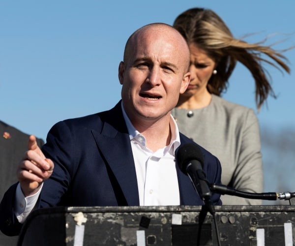 max rose in a navy blue suit and white shirt speaking at a podium outside