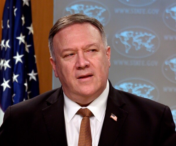 pompeo in a black suit and brown tie in front of a projection of the state department logo