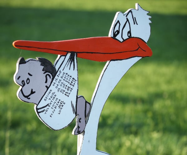 A wooden sign of a stork carrying a baby