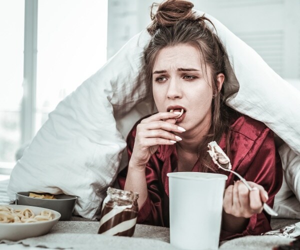 woman in bed looking stressed/depressed eating ice cream and other junk foods