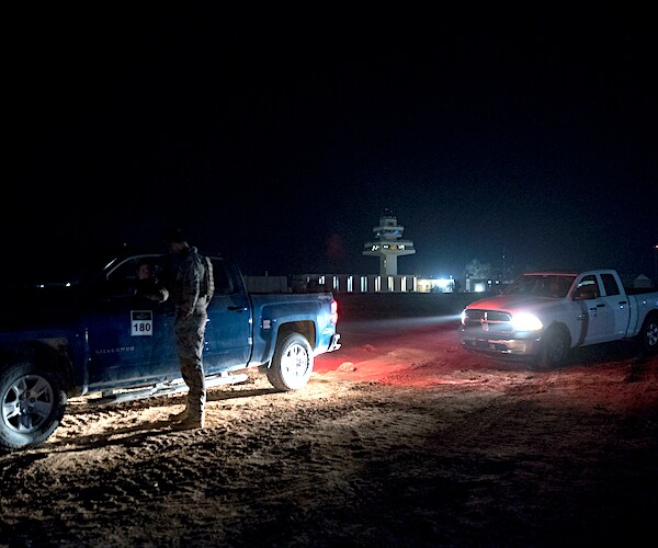 officials on guard outside of al assad airbase in iraq in the dead of night, lighted only by truck headlights