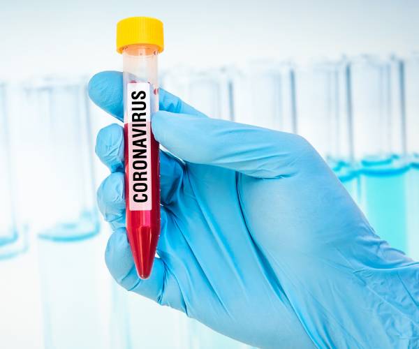 gloved hand holding a test tube with blood labeled coronavirus