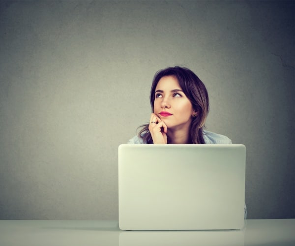 woman sitting at table with laptop and daydreaming