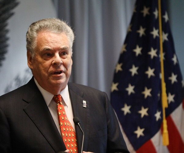 peter king in a patterned orange tie and dark gray suit in front of an american flag