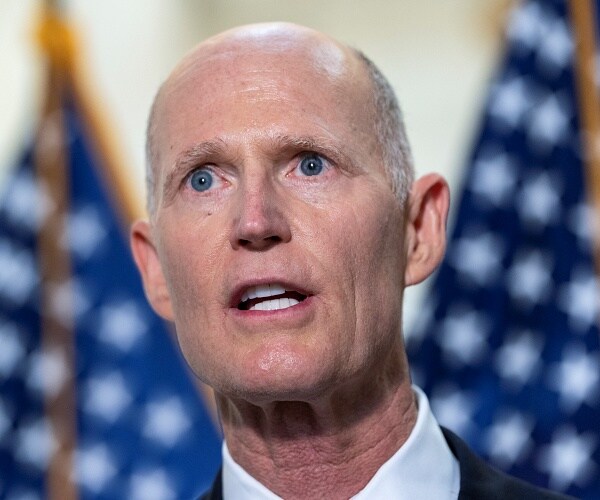 rick scott stands in front of american flags