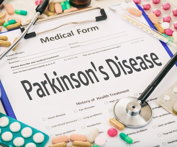 Medical form on a clipboard with diagnosis of Parkinson's disease, pills and stethoscope around it