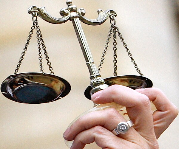 the scales of justice are held up by a hand with a ring on its finger