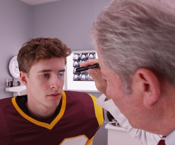 doctor looking in eyes of teen football player