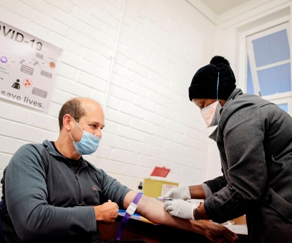 nurse wears a mask and draws blood from a man's arm while he sits in a chair