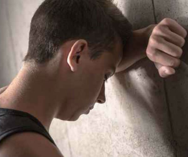 a sad teen, with head down, leaning on a wall 