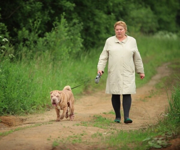 an overweight woman walking a dog along a trail