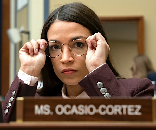 alexandria ocasio-cortez puts on and adjusts her glasses as she sits before a house committee hearing