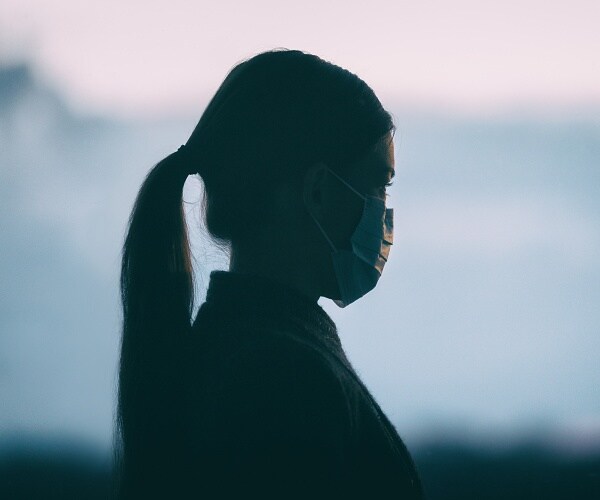 woman wearing mask looks out window