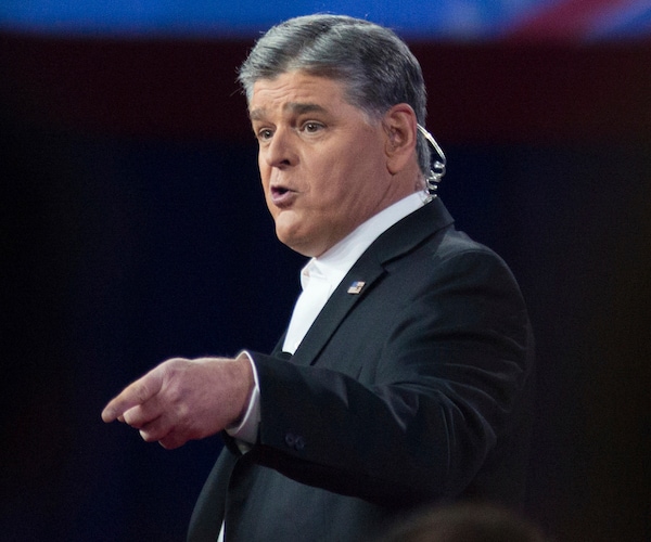 sean hannity, wearing an ear piece, looks left and points left and down with his left index finger