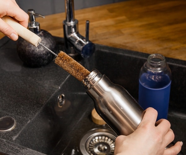 person cleaning a reusable water bottle in sink