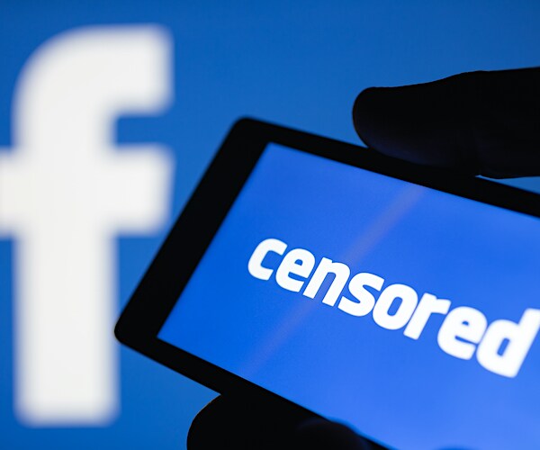 a man holds a smart phone with the word censorship on it, in front of the facebook logo