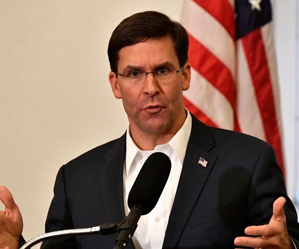 esper in a black suit and white shirt speaking in front of an american flag