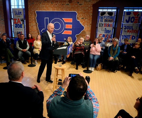 joe biden speaking in the middle of a room with a cutout of iowa with his name on it