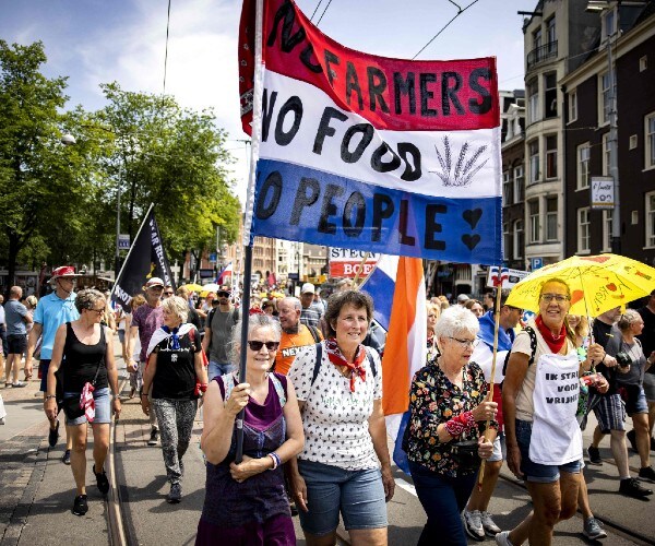 marchers in the street with one carrying a netherlands flag with the words no farmers no food no people written on it