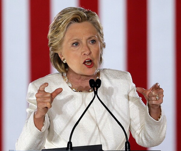 hillary clinton gestures with both hands while delivering a speech in front of a large american flag in the background