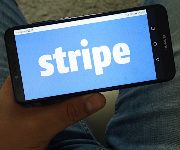 a man wearing blue jeans holds a smart phone in his lap with stripe logo shown on it