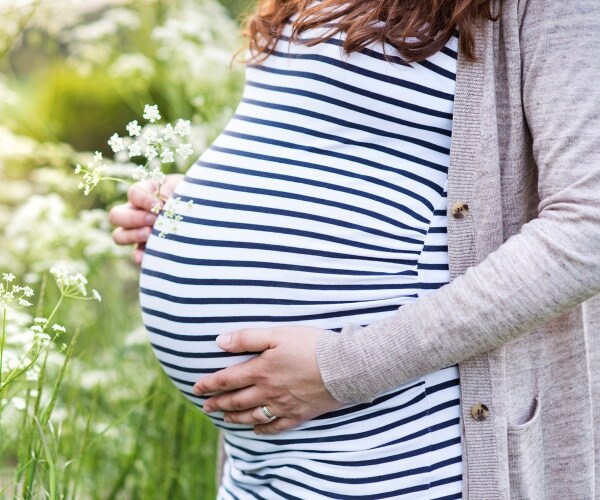 woman in a striped dress and cardigan holds her pregnant belly