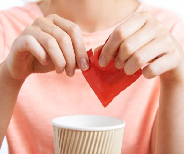 woman opening artificial sweetener packet above coffee cup