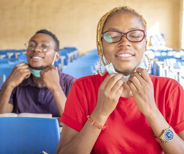 two students take off their medical masks and smile in a classroom