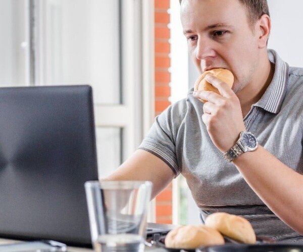 Business man eating a roll while working on laptop