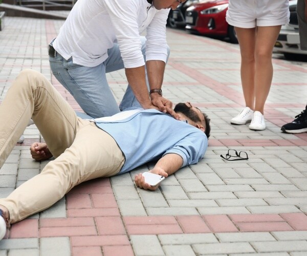 person performing CPR on man on ground on street