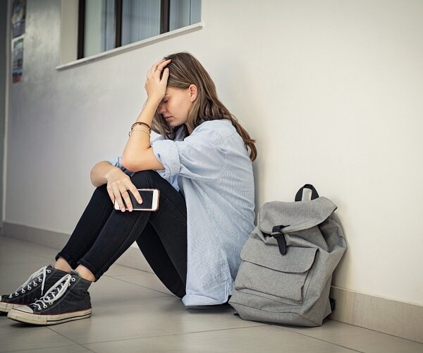 upset teenage girl sitting alone in hallway