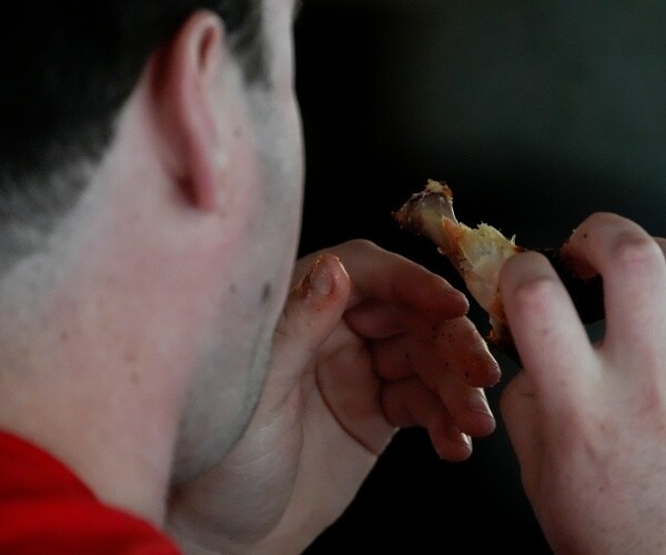 man eating chicken wing with hands