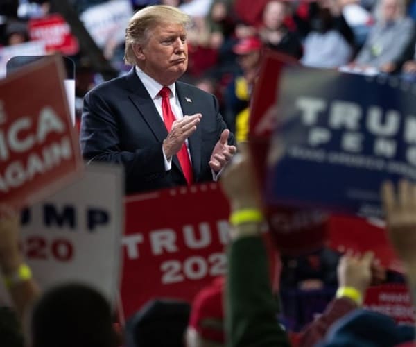 president trump claps from stage at one of his campaign rallys.