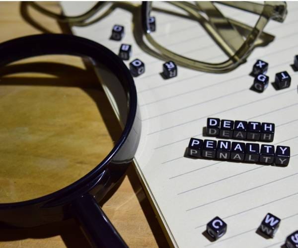 death penalty spelled out in small blocks on a legal pad with a magnifying glass and reading glasses lying nearby