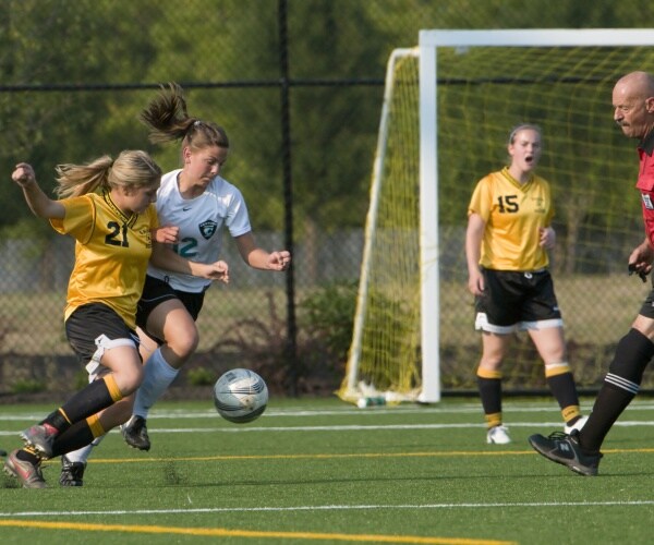 two girls on different high school soccer teams fighting for ball