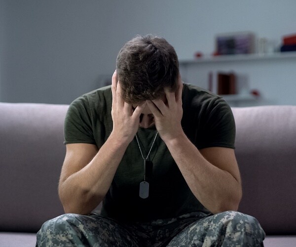 male soldier sits on couch with head in his hands