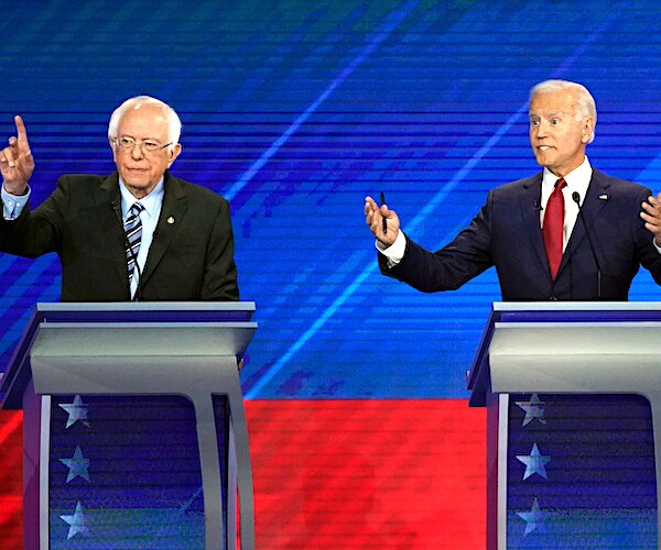 bernie sanders raises his hand while joe biden exults during a democratic presidential primary debate